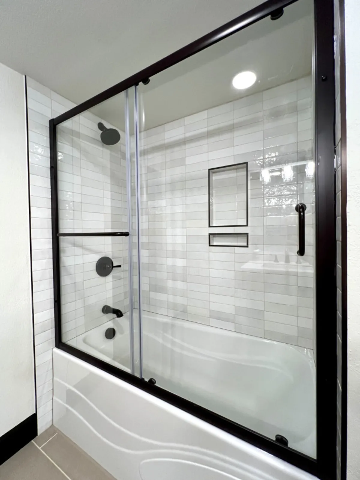 A modern bathroom featuring a glass shower enclosure, black fixtures, white tiled walls, and a sleek bathtub. The clean lines and tranquil palette create a serene atmosphere ideal for self-care routines.