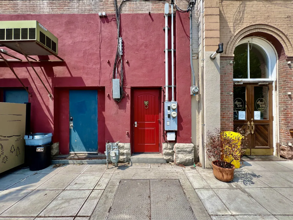 A quirky and inviting streetscape with a red door and blue door, accented by yellow planters and artistic touches. The setting invites exploration and hints at the area’s hidden gems and local character.