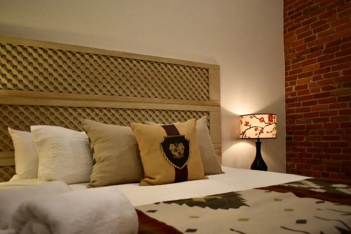 A serene bedroom scene featuring a decorative headboard, intricately designed pillows, and a floral-patterned lamp. The soft morning light gently illuminates the cozy setup, conveying a sense of comfort and relaxation ideal for restful sleep.