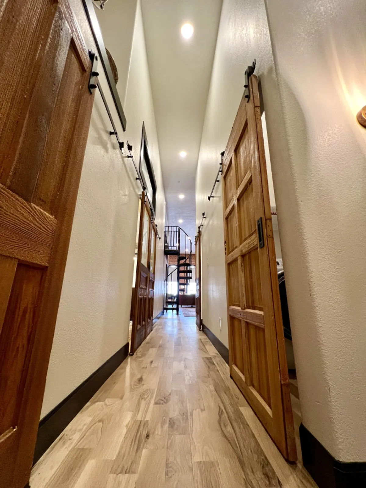 A long, welcoming hallway accented by wooden sliding doors and a striking spiral staircase. The scene captures lively family moments and the promise of exploration within the apartment, with laughter and casual conversations echoing down the corridor.